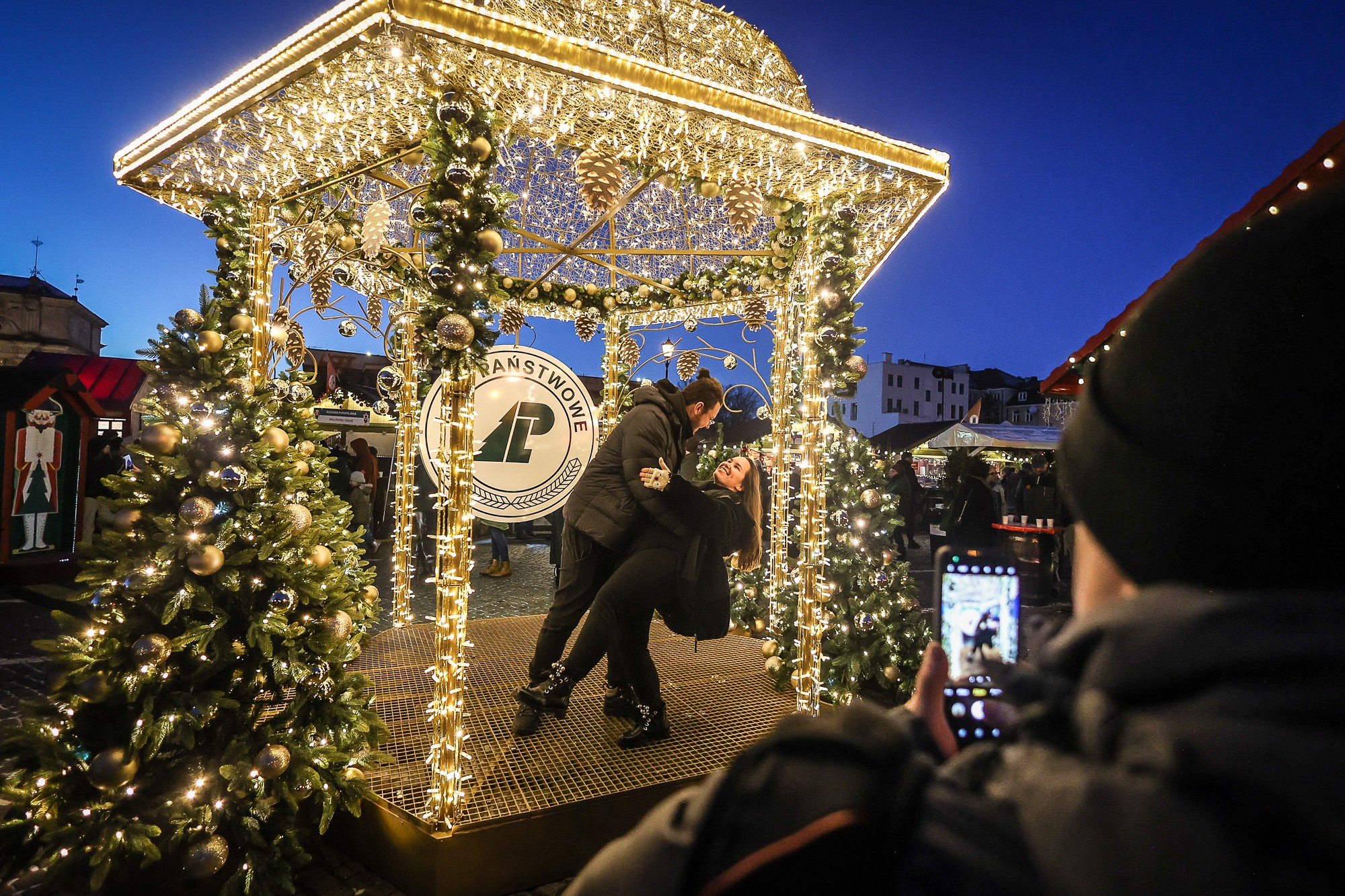 Para tańczy w oświetlonej światełkami altanie Lasów Państwowych na Jarmarku Bożonarodzeniowym w Gdańsku